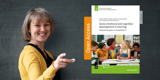 9. SYM-Herausgeberband Eine Lehrkraft lächelt zur Kamera und deutet auf das Cover des 9. SYM-Herausgeberbandes